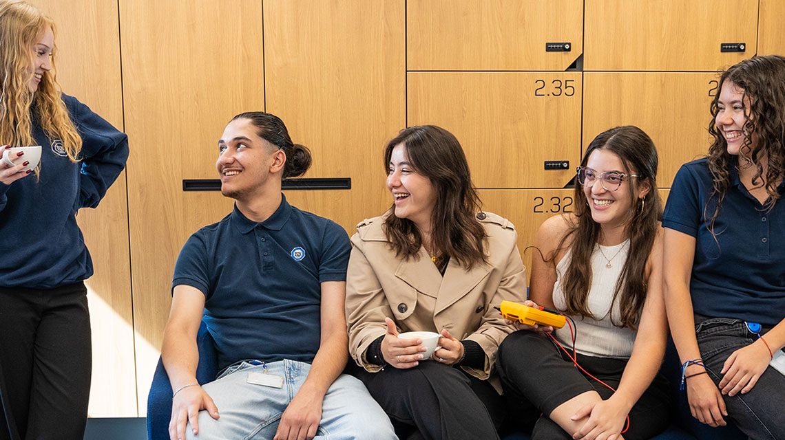A group of young people chilling on a sofa in an office environment, talking and laughing.