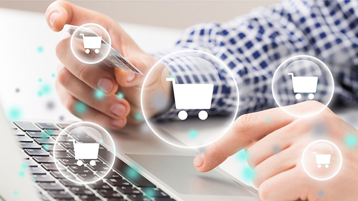 A person using a laptop, holding a credit card while clicking on the trackpad, with digital shopping cart icons floating around.