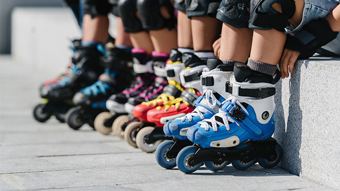 A row of people wearing rollerblades and protective gear, such as knee pads and elbow pads.