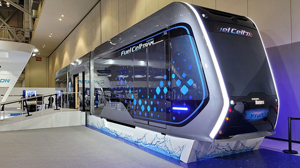 A sleek, futuristic hydrogen fuel cell train displayed in an exhibition hall, showcasing advanced transportation technology with a modern design and blue geometric patterns on its side.