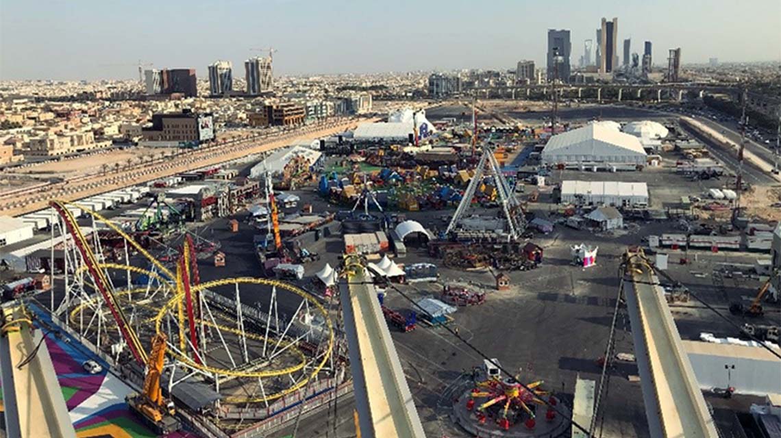 The grounds of an amusement park, photographed from above, with the skyline of a city in the background.
