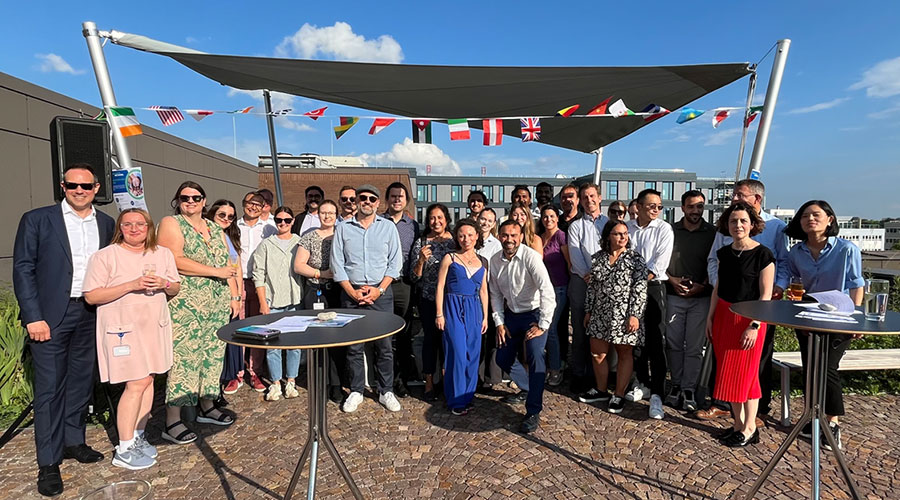 A diverse group of people standing on a rooftop terrace, smiling at the camera.