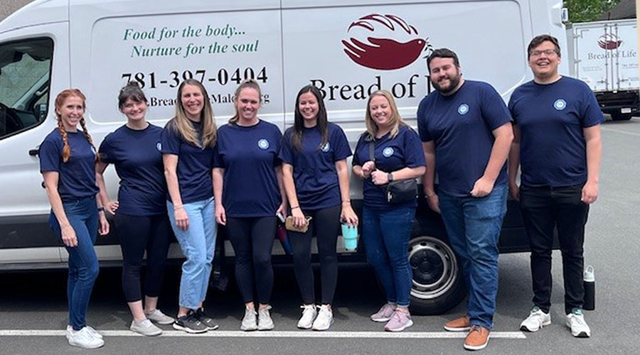 A group of people wearing TÜV SÜD T-shirts stand in front of a mini-truck and smile for the camera.