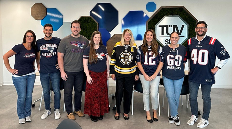 A happy group of people standing in front of a large TÜV SÜD logo, wearing football shirts.