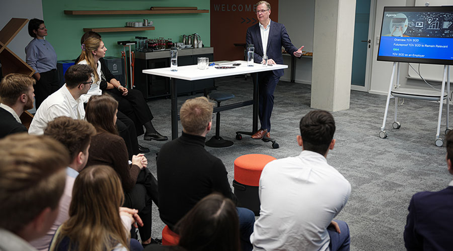 A man in a dark suit presenting to a young crowd.