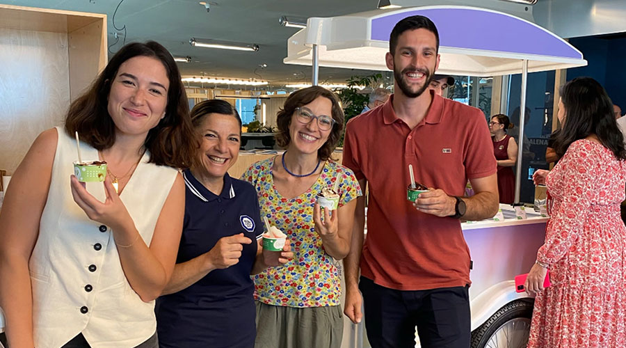 A group of people having a small cup of ice cream in an office environment with big smiles on their faces.