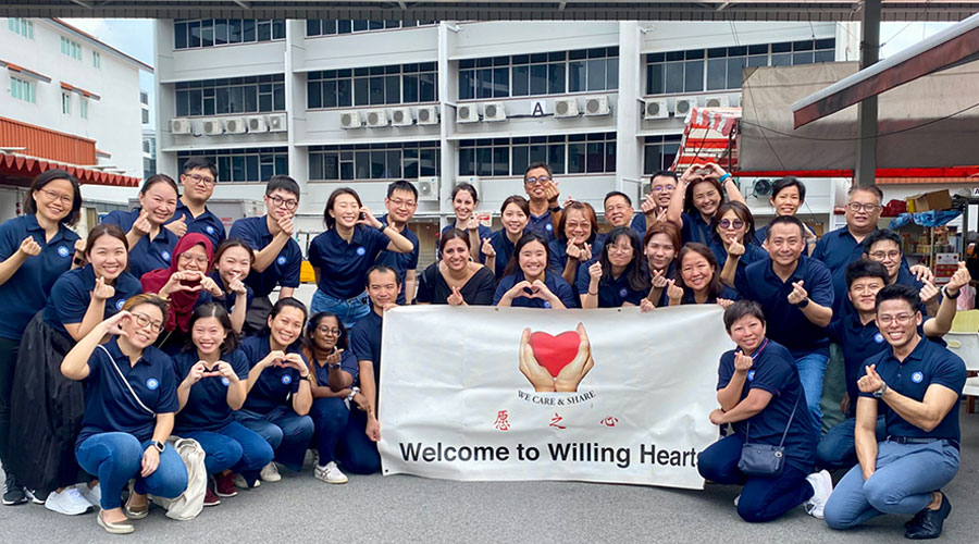 A large crowd standing together, smiling and making the shape of a heart with their hands.